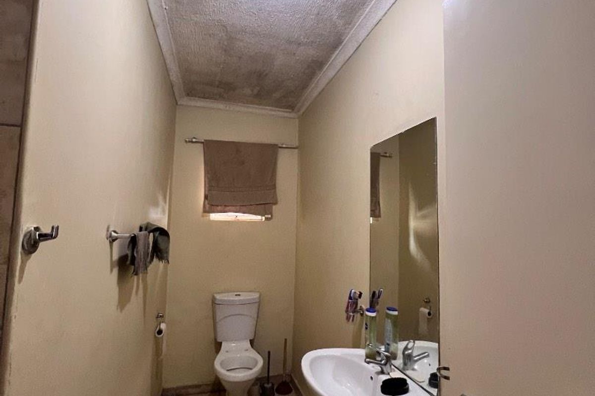 A compact bathroom featuring a pedestal basin, toilet, and tiled flooring, currently showing signs of ceiling water damage and wear.