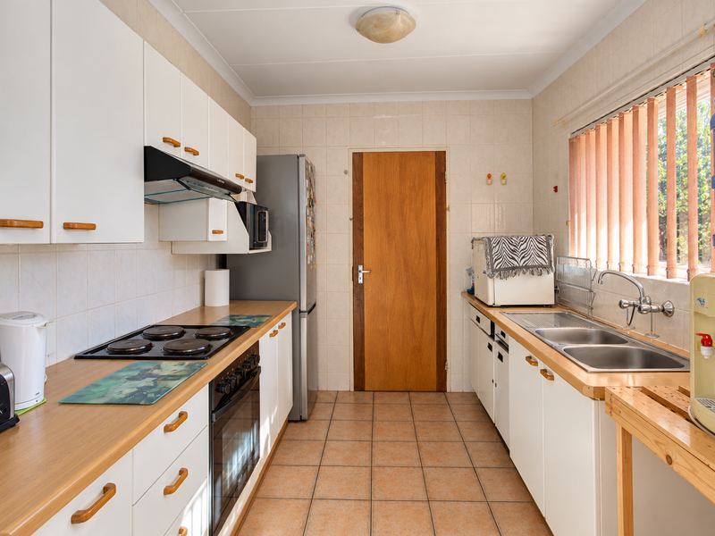 A functional kitchen featuring white cabinetry, laminate countertops, an electric hob, built-in oven, and a double stainless steel sink with tiled finishes.