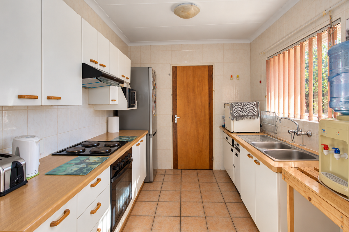 A functional kitchen featuring white cabinetry, laminate countertops, an electric hob, built-in oven, and a double stainless steel sink with tiled finishes.