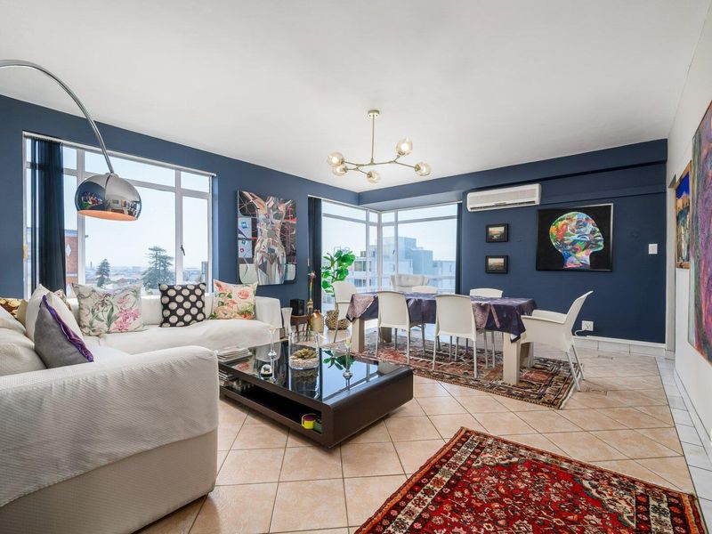 Spacious open-plan living and dining area featuring tiled floors, large windows with natural light, and a wall-mounted split-system air conditioner.
