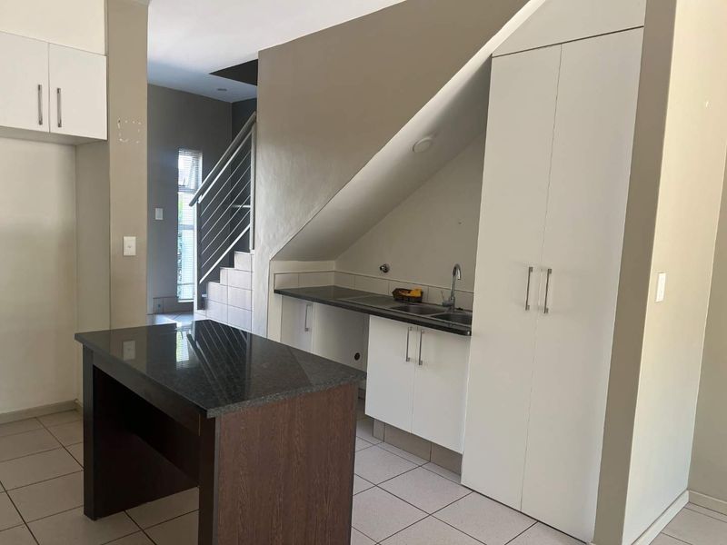A functional kitchen area featuring built-in cabinetry, granite countertops, a central island, and an integrated staircase, offering a clean and practical layout.