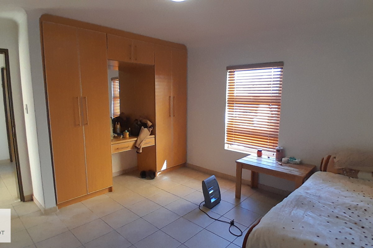 A bedroom featuring built-in wooden cupboards with an integrated vanity, tiled flooring, and a window fitted with venetian blinds.