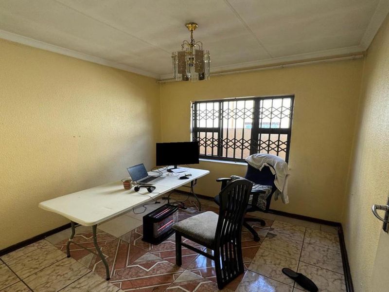 A functional office space featuring tiled flooring, security bars on the window, and a central ceiling light fixture.