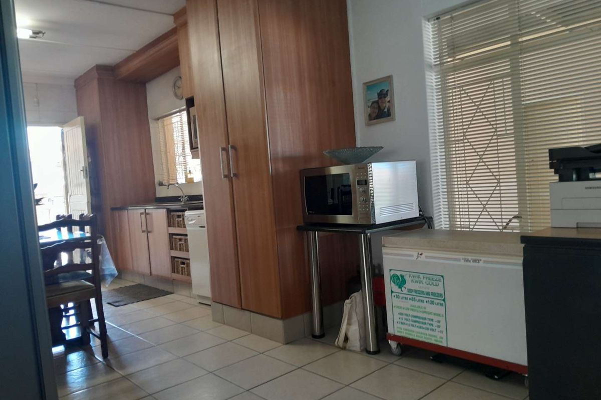 A functional kitchen area featuring wood-look cabinetry, tiled flooring, and a window with fitted blinds, providing a practical workspace.