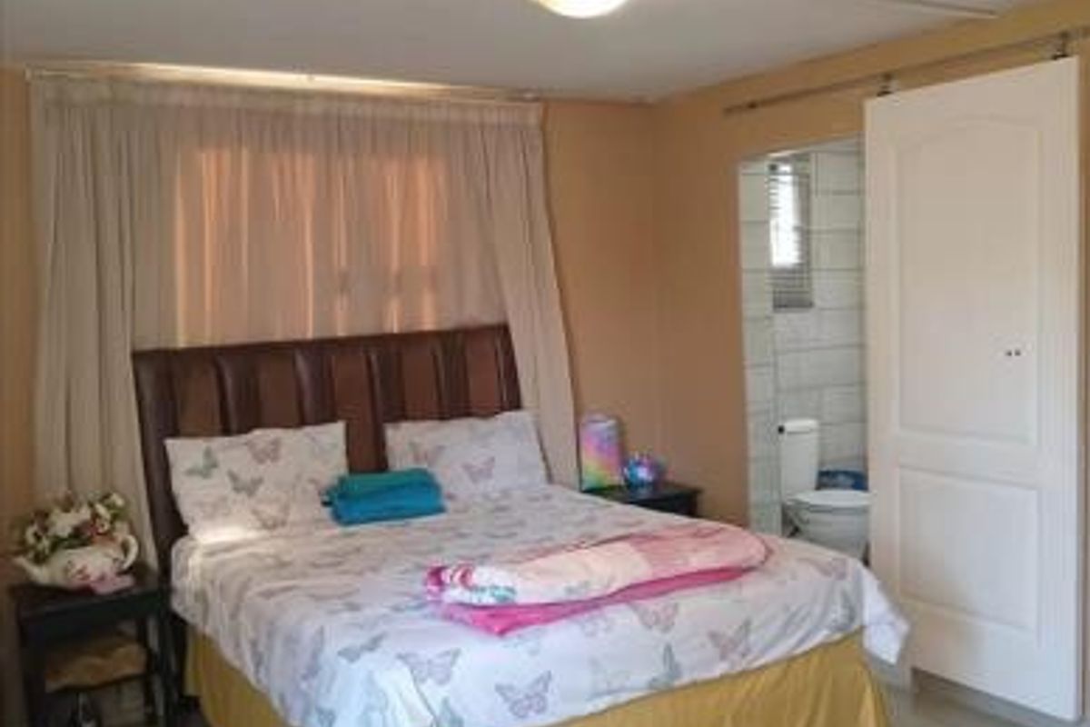 A bedroom featuring tiled flooring, a sliding door, and direct access to an en-suite bathroom, with exposed electrical conduit visible on the ceiling.