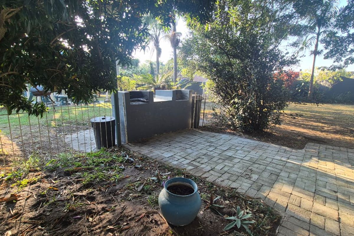 A rear garden area featuring a paved patio space with a built-in brick braai and perimeter wire fencing.