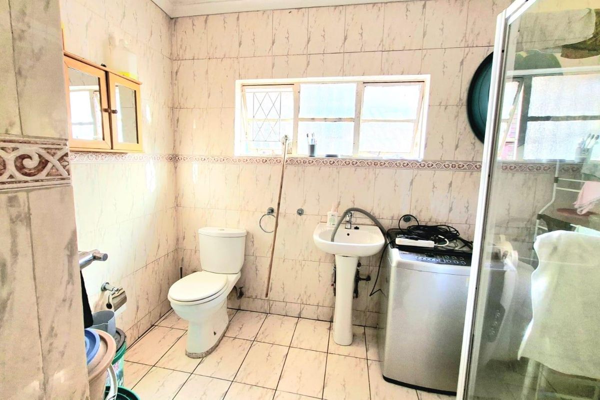 A functional bathroom featuring a pedestal basin, toilet, and shower enclosure with floor-to-ceiling wall tiling.