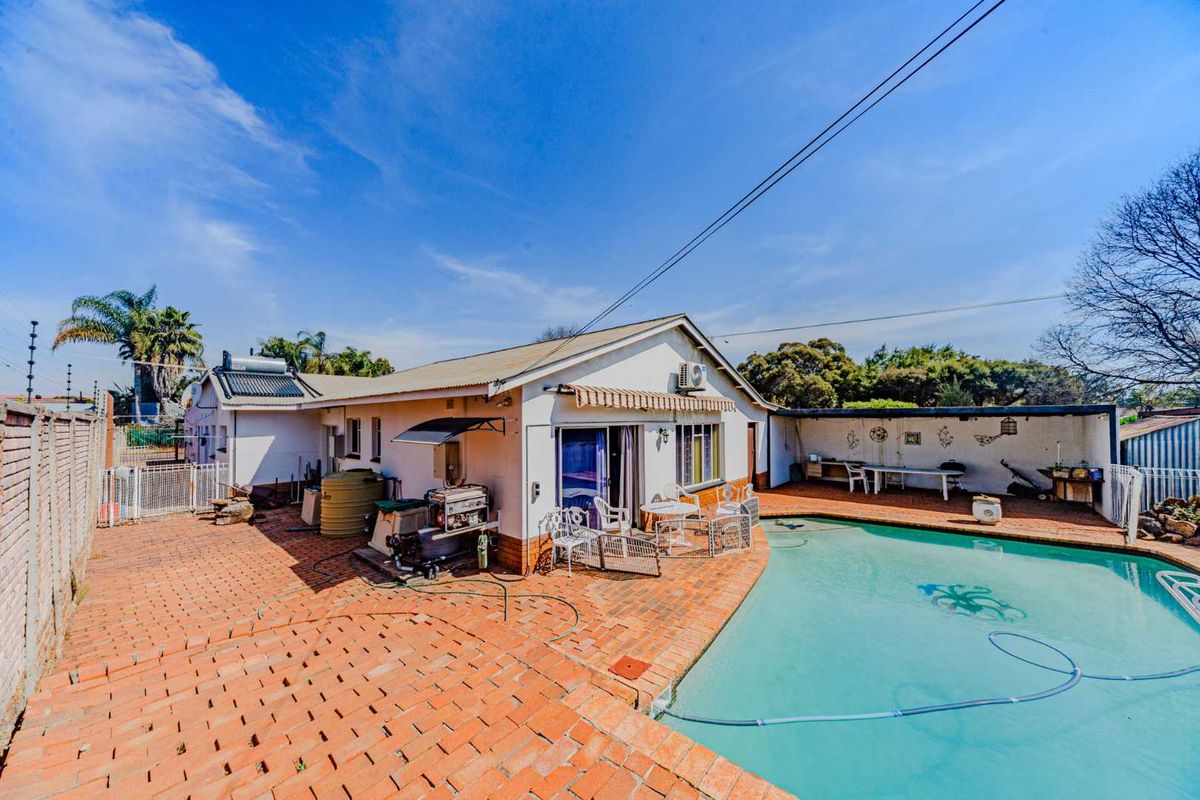 Rear exterior view featuring a swimming pool, brick paved patio area, and covered outdoor space with solar water heating infrastructure.