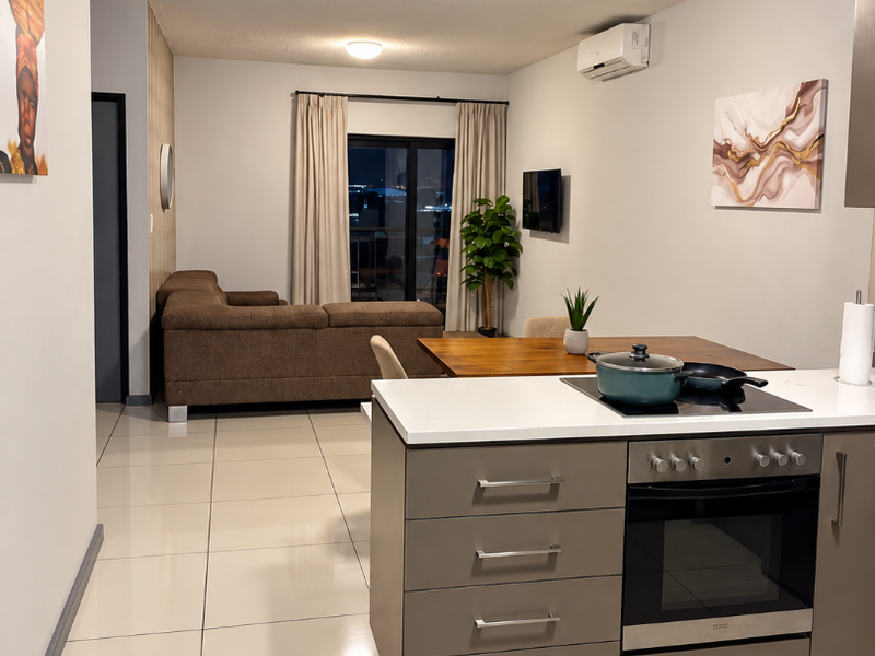 Modern open-plan living area featuring a sleek kitchen with built-in oven, stone countertops, and tiled flooring, seamlessly flowing into the lounge space.