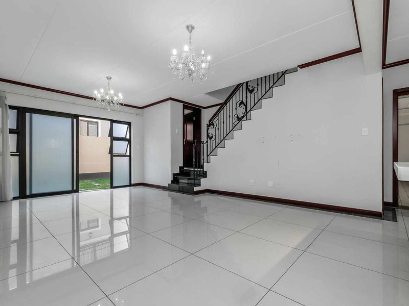 Spacious, light-filled living area featuring polished tile flooring, elegant wrought iron staircase detailing, and direct access to the outdoor space through sliding glass doors.