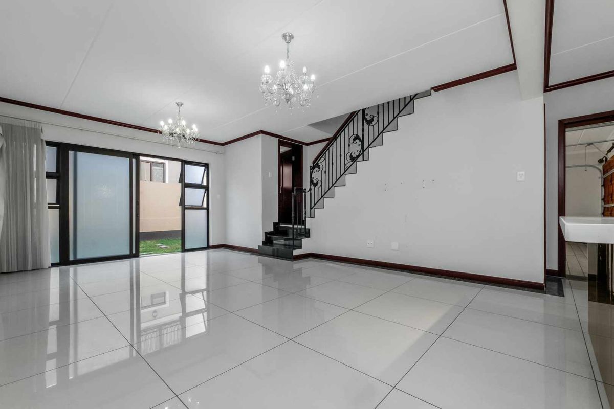Spacious, light-filled living area featuring polished tile flooring, elegant wrought iron staircase detailing, and direct access to the outdoor space through sliding glass doors.