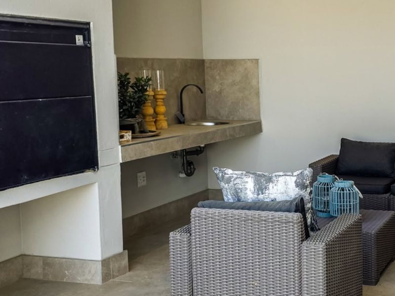 Covered patio area featuring a built-in braai, concrete prep counter with integrated sink, and neutral tiled flooring.