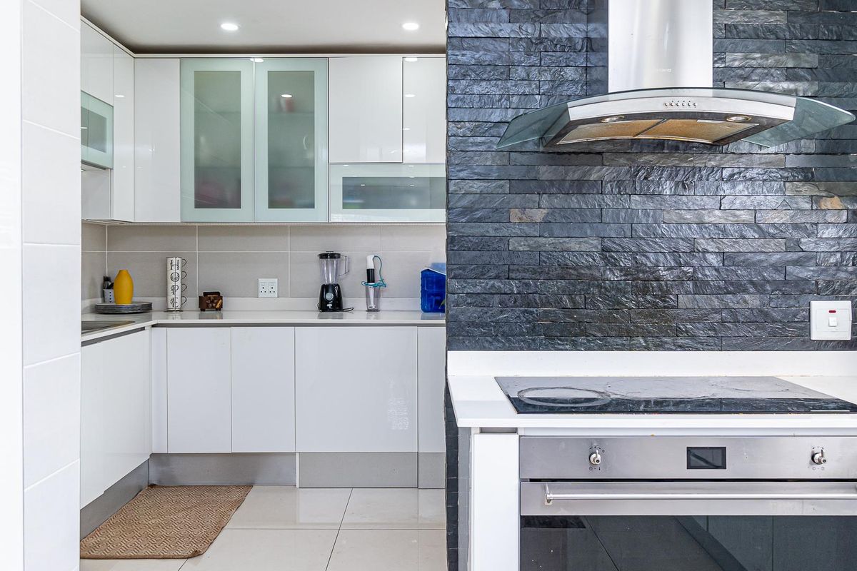 Modern kitchen featuring white cabinetry, stone-tiled feature wall, built-in oven, glass extractor fan, and sleek countertops.