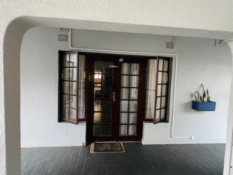 Covered entrance area featuring timber-framed glass double doors and matching casement windows, providing a classic aesthetic to the apartment entry.