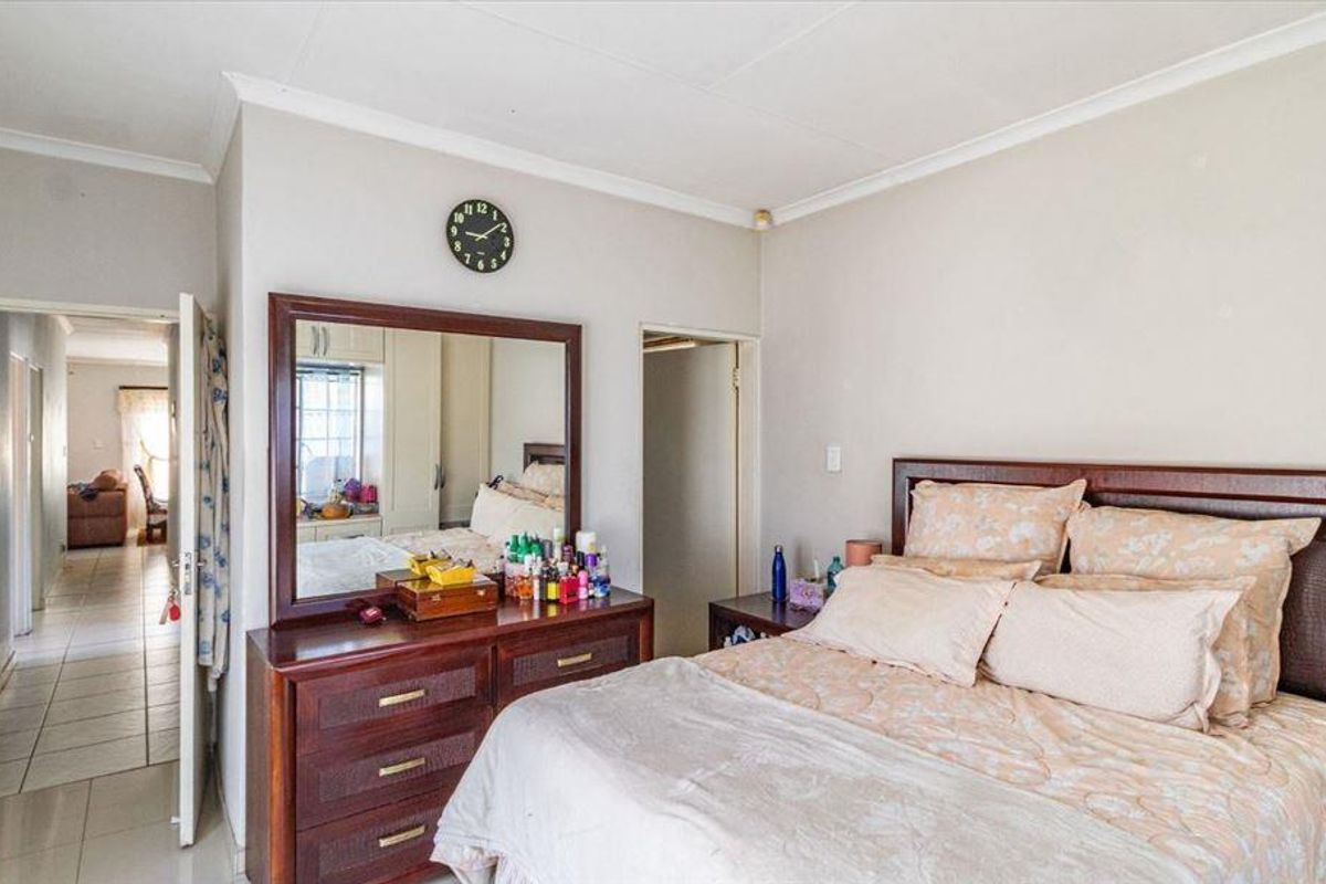 A well-lit bedroom featuring tiled flooring, coved ceilings, and a doorway leading to an adjacent hallway.