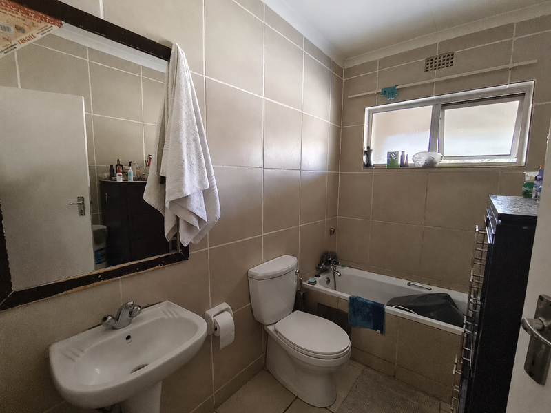 A functional bathroom featuring a pedestal basin, toilet, and bathtub with full-height wall tiling and a window for natural light.