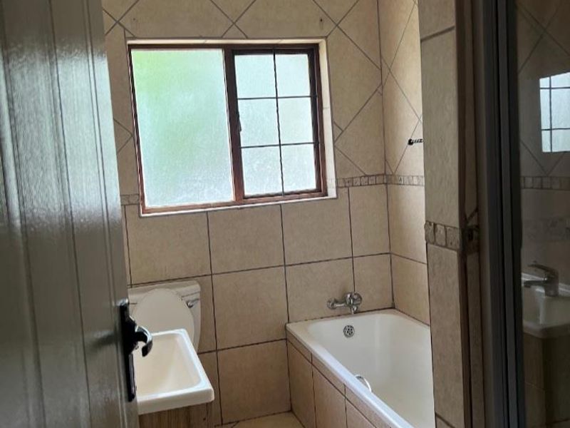 A functional bathroom featuring a built-in bathtub, separate shower enclosure, vanity cabinet, and neutral tiled finishes throughout.