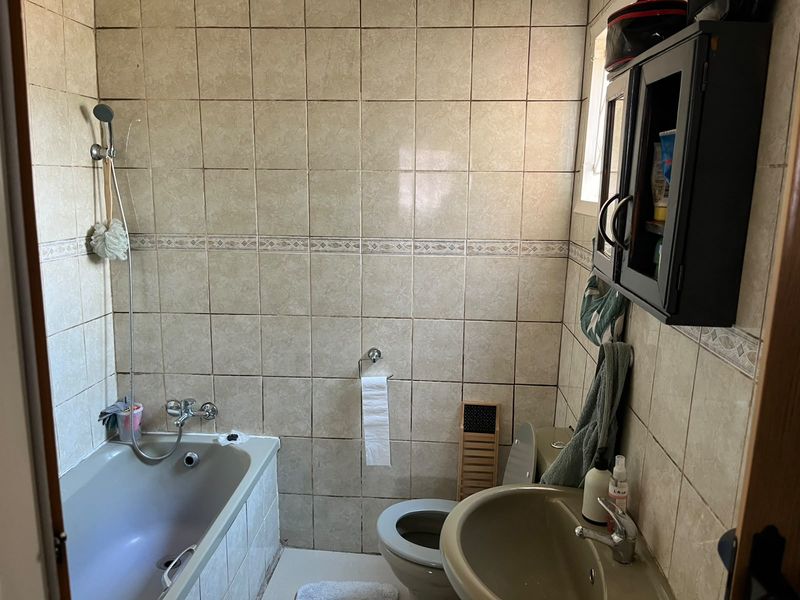 A compact bathroom featuring full-height wall tiling, a bathtub with shower mixer, a pedestal basin, and a toilet, offering potential for modern renovation.