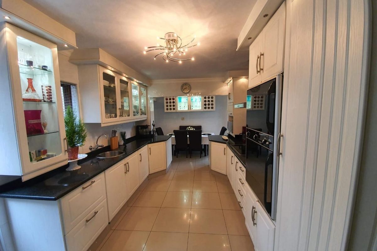 A well-maintained kitchen featuring white cabinetry, dark granite countertops, integrated oven, and tiled flooring, leading into a dining area.