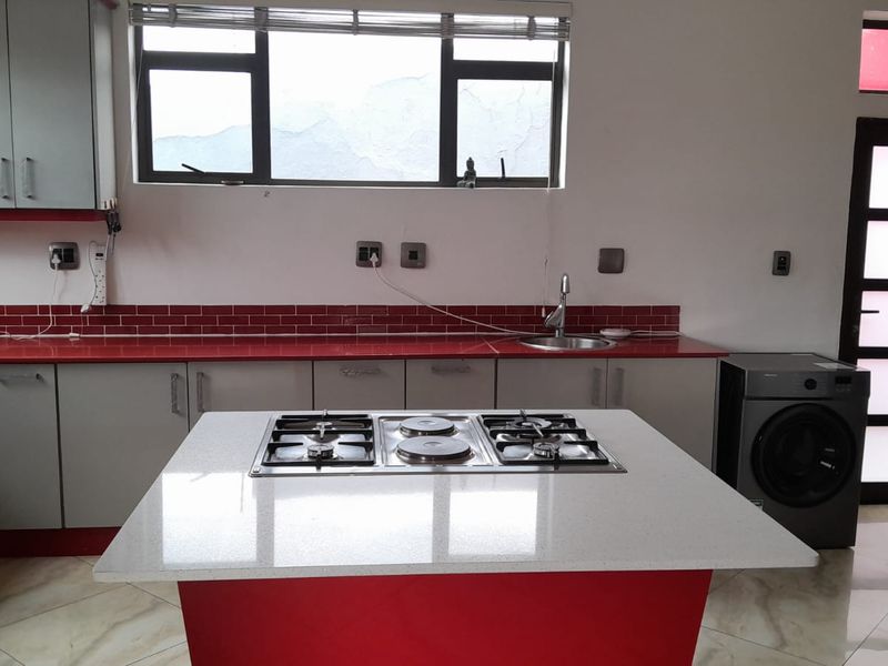 Modern kitchen featuring a central island with integrated gas and electric hobs, stone countertops, tiled backsplash, and ample fitted cabinetry.
