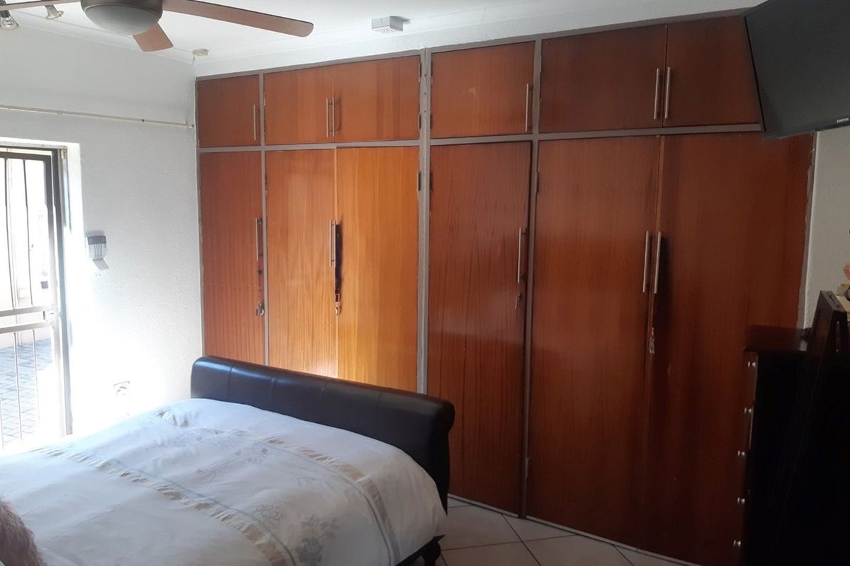 Bedroom featuring extensive built-in wooden cupboards, tiled flooring, and a ceiling fan, with direct access to an outdoor area via a sliding door.
