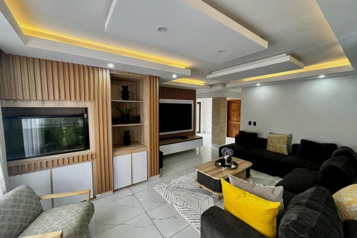 Modern living room featuring a custom timber-slat feature wall with integrated shelving, recessed tray ceilings with ambient lighting, and polished porcelain floor tiles.