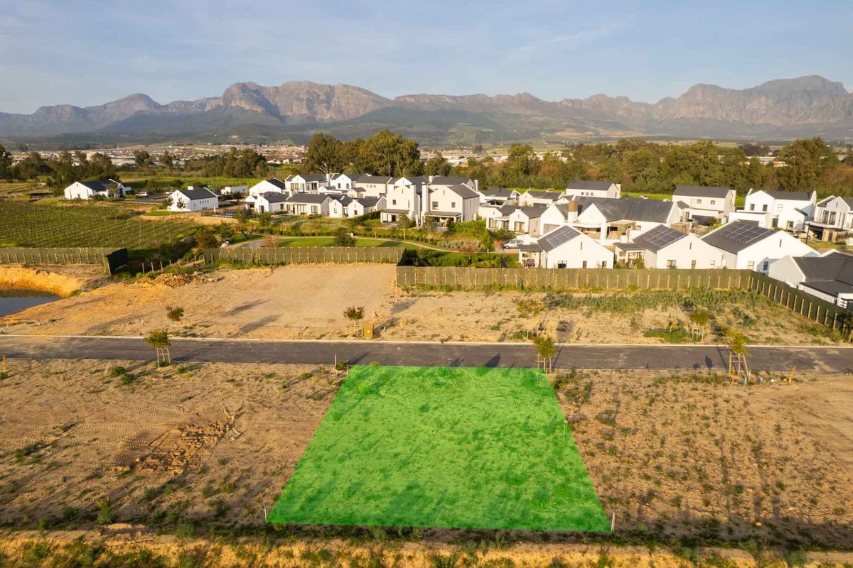 An aerial view of a vacant residential plot in a developed estate, featuring mountain views and established surrounding infrastructure.