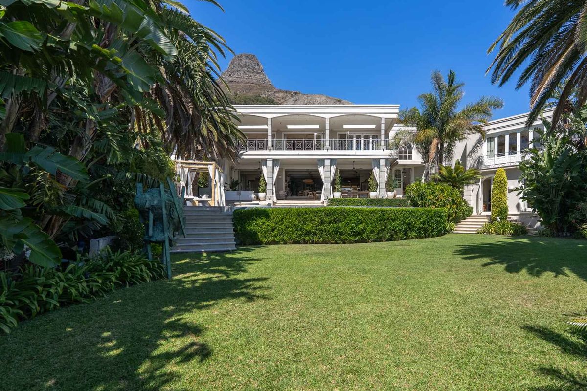 A beautifully maintained rear garden featuring a lush lawn, mature landscaping, and a spacious covered patio with balcony access overlooking the property.