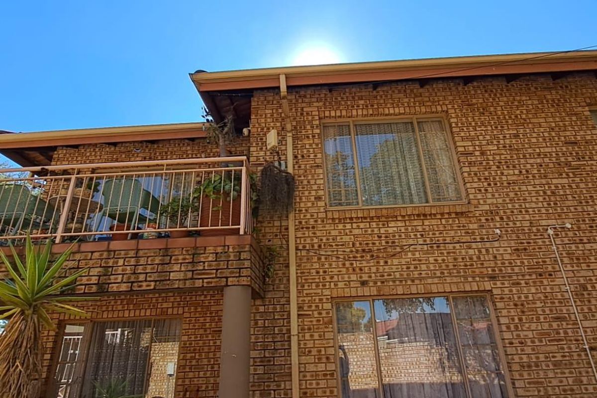Rear view of a double-story townhouse featuring face-brick facade, a private balcony with metal railing, and large windows.