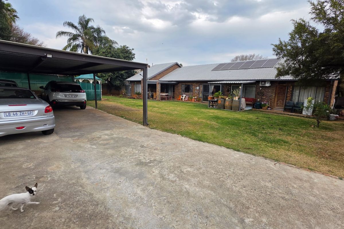 Rear view of the property featuring a spacious lawn, a covered carport, and solar panels installed on the tiled roof.
