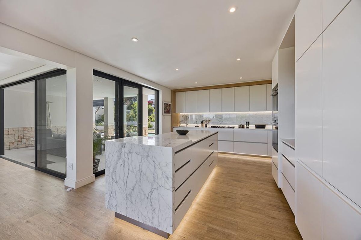 Modern open-plan kitchen featuring a large marble-topped island, sleek handleless cabinetry, integrated appliances, and seamless flow to the outdoor patio area.