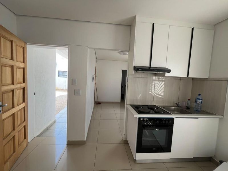 Compact kitchen featuring modern white cabinetry, built-in electric oven and hob, extractor fan, and tiled flooring, with direct access to an outdoor area.