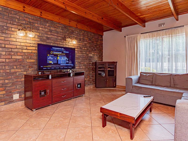 A living room featuring an exposed brick feature wall, timber beam ceiling, and tiled flooring with access to the outdoors via a sliding door.