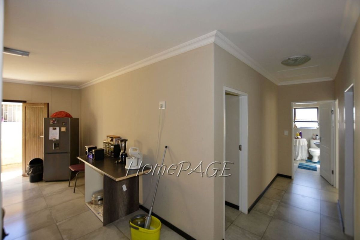 Interior view showing a tiled living area with access to a hallway and bathroom, featuring neutral wall tones and crown molding.