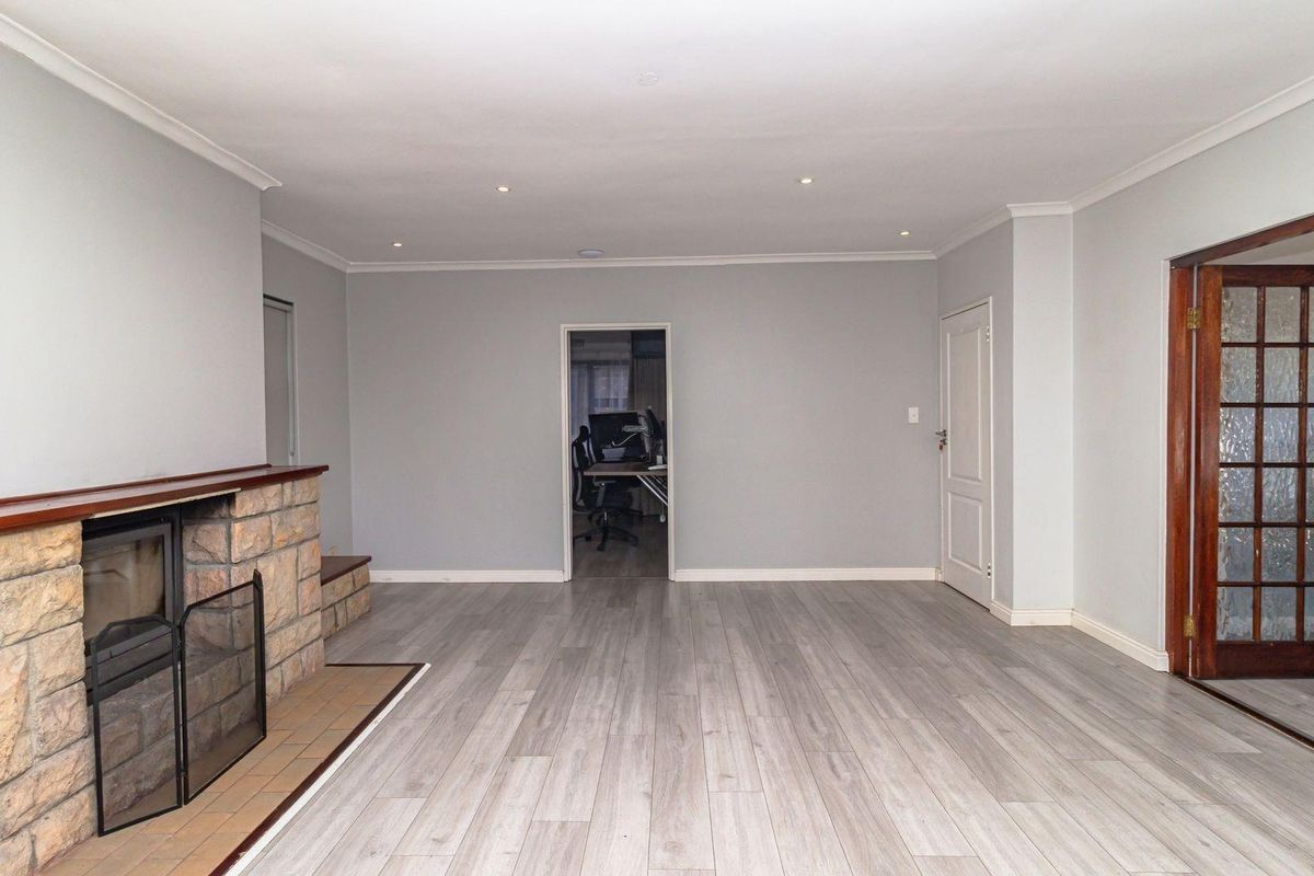 Spacious living room featuring light wood-look flooring, a stone-clad fireplace, and classic wooden French doors leading to an adjacent room.