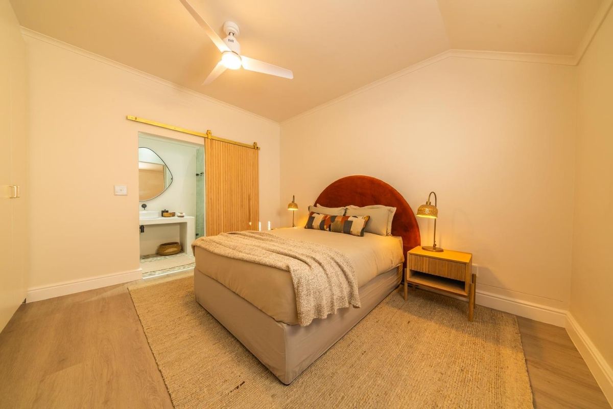 A well-maintained bedroom featuring light wood-look flooring, a ceiling fan, and a sliding barn door providing access to an en-suite bathroom.
