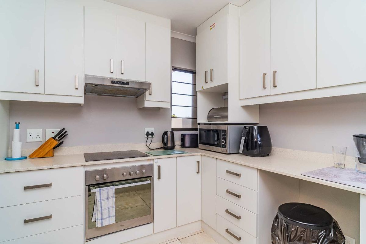 A compact, modern kitchen featuring white cabinetry, stone-look countertops, a built-in oven, electric hob, and stainless steel extractor fan.