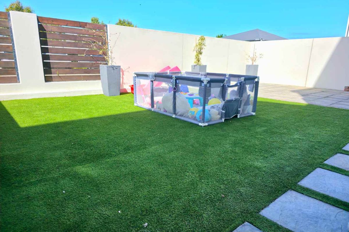 A private, low-maintenance courtyard featuring artificial turf, paved pathways, and high perimeter walls with timber slat screening for added privacy.