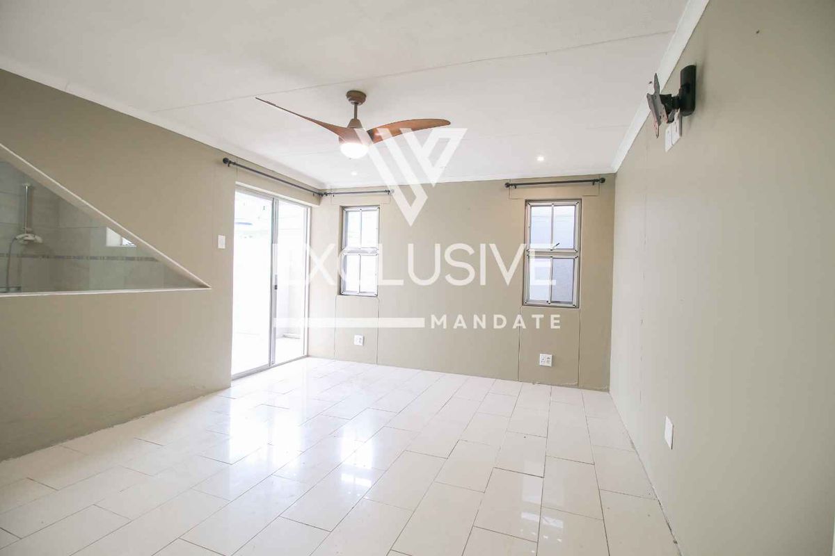 A bright, empty living area featuring tiled flooring, a ceiling fan, and sliding glass doors providing access to the exterior.