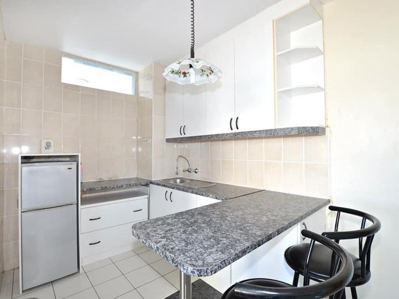 Compact kitchen featuring white cabinetry, laminate countertops, tiled backsplash, and a breakfast bar area with tiled flooring.