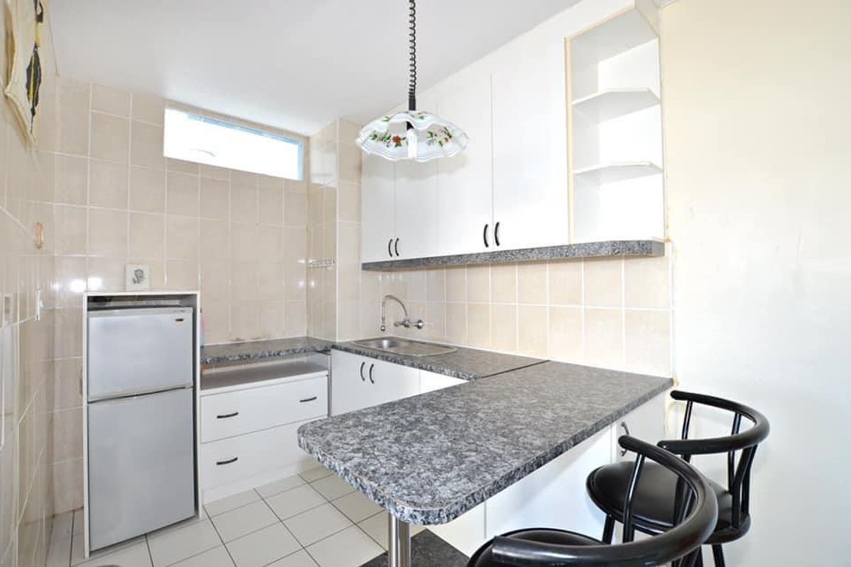 Compact kitchen featuring white cabinetry, laminate countertops, tiled backsplash, and a breakfast bar area with tiled flooring.