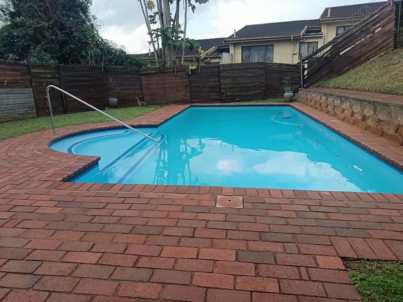 Outdoor swimming pool area featuring brick paving, a retaining wall, and perimeter timber fencing.