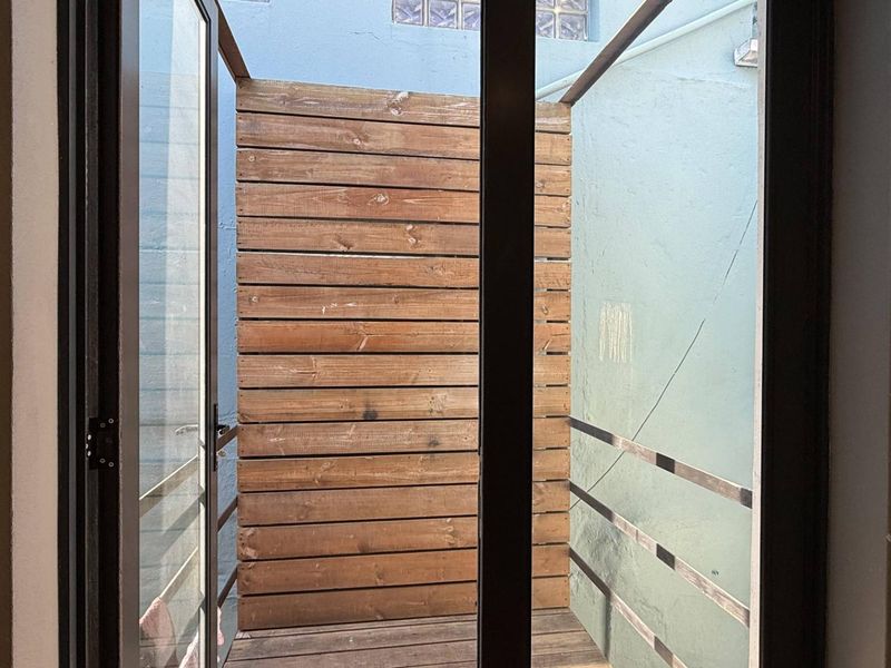 A small, private outdoor balcony featuring timber decking and a wooden privacy screen, accessible through a glass door.