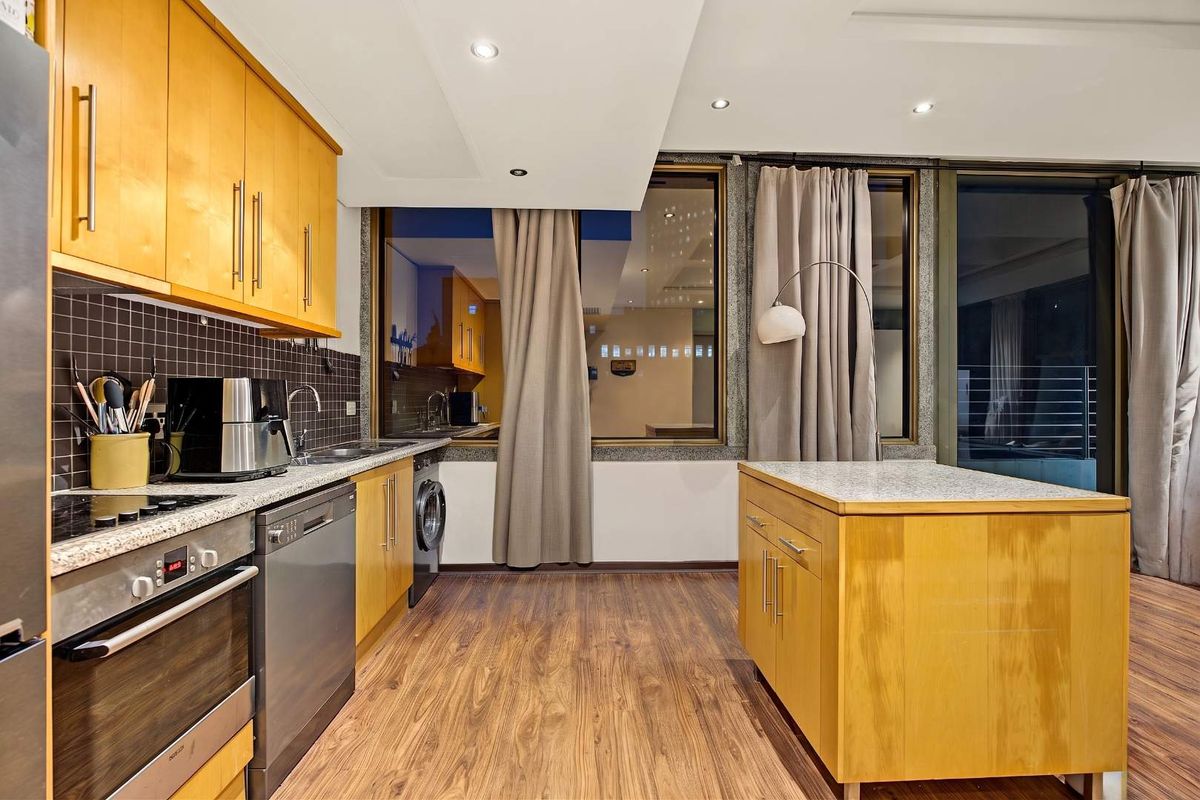 Modern kitchen featuring light wood cabinetry, granite countertops, integrated appliances, and laminate flooring, with large windows providing natural light and a contemporary feel.