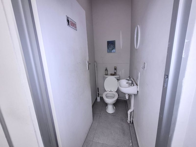A compact gents restroom featuring a standard toilet, wall-mounted basin with exposed plumbing, and tiled flooring.