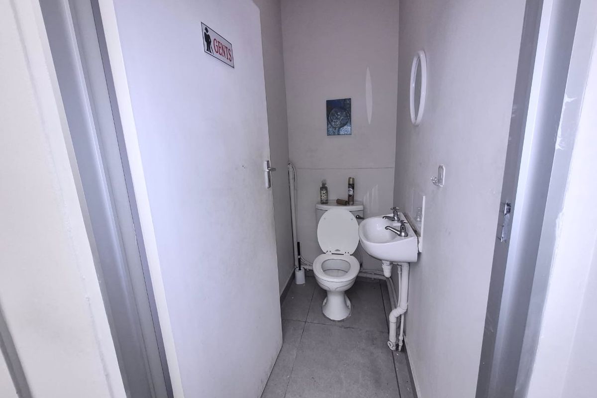 A compact gents restroom featuring a standard toilet, wall-mounted basin with exposed plumbing, and tiled flooring.