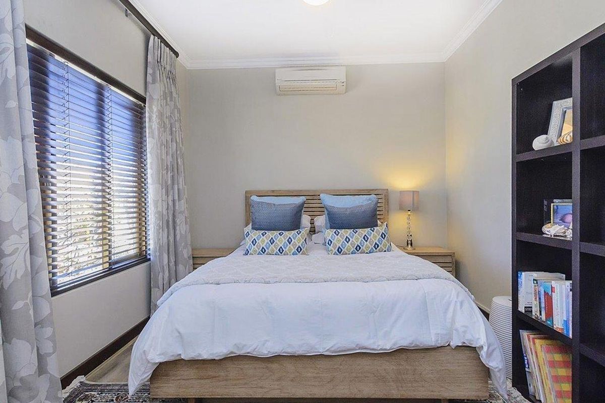 A well-maintained bedroom featuring a wall-mounted air conditioning unit, crown molding, and large windows with fitted blinds.