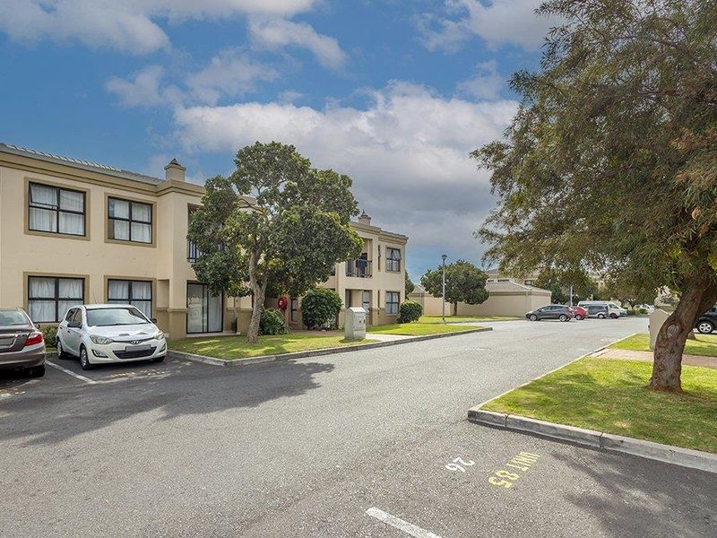 Exterior view of a multi-story apartment complex featuring paved parking areas, landscaped green spaces, and balconies.