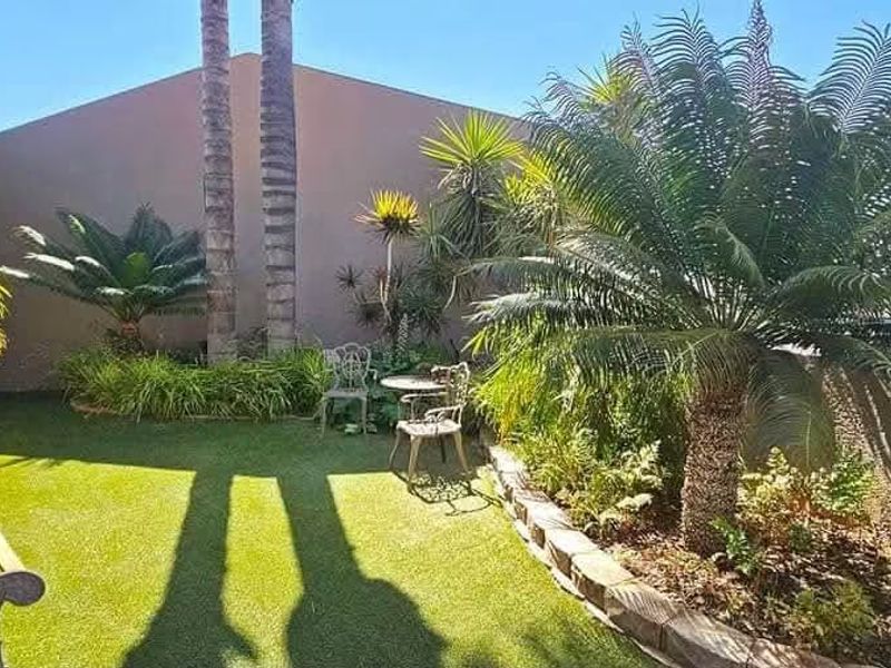 A well-maintained garden area featuring artificial turf, established palm trees, and a stone-edged retaining wall, offering a pleasant outdoor space.