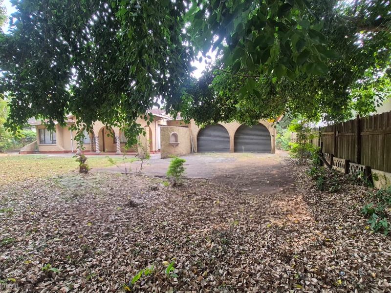 Front view of a residential property featuring a double garage, arched entrance with decorative columns, and a large, unmaintained garden area.